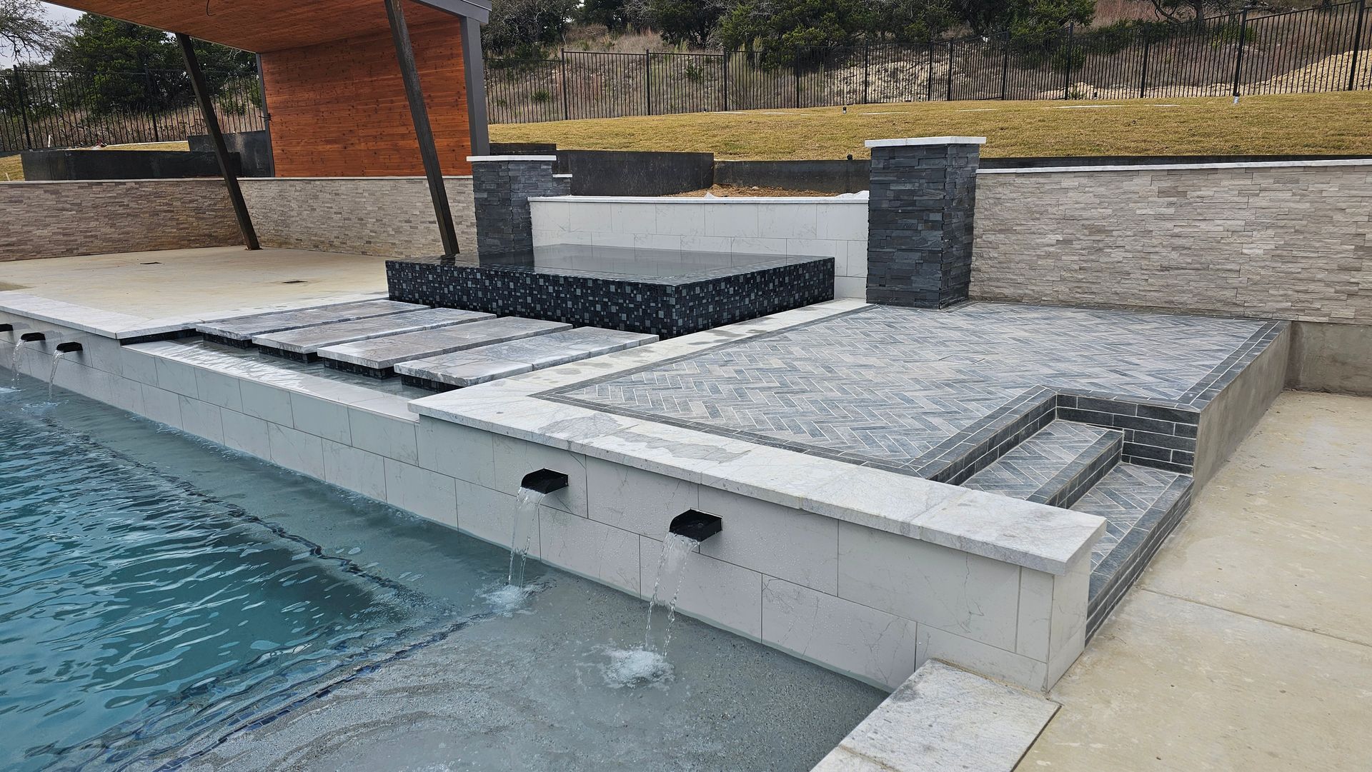 Custom gunite pool with raised black glass-tile spa and stone patio overlooking the Hill Country in Caliza Reserve, Boerne TX